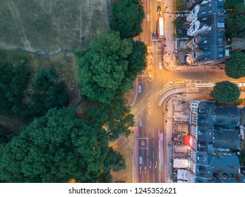 Birds eye view of light trails over busy south west London intersection with green trees and historic townhouses at night - September 2018