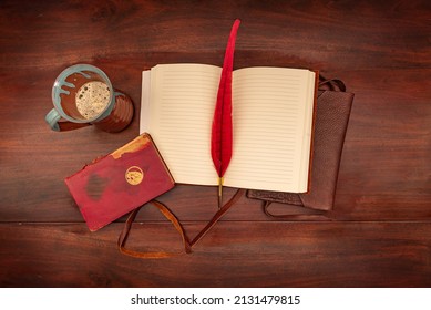 Birds Eye View Of An Open Leather Diary On An Antique Table With A Red Quill Pen And A Coffee Mug Beside A Red Book