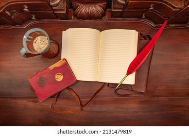 Birds Eye View Of An Open Leather Diary On An Antique Table With A Red Quill Pen And A Coffee Mug Beside A Red Book