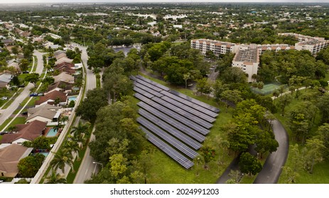 A Bird's Eye View Over Rows Of Solar Panels In A Suburban Neighborhood. The Panels Are Surrounded By Green Grass And Trees. It Is A Cloudy Day In Florida.