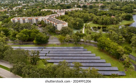 A Bird's Eye View Over Rows Of Solar Panels In A Suburban Neighborhood. The Panels Are Surrounded By Green Grass And Trees. It Is A Cloudy Day In Florida.