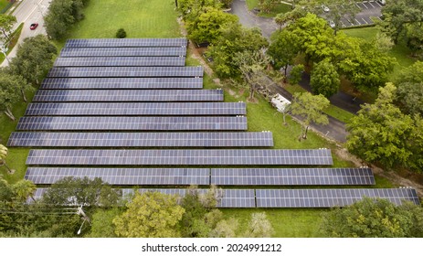 A Bird's Eye View Over Rows Of Solar Panels In A Suburban Neighborhood. The Panels Are Surrounded By Green Grass And Trees. It Is A Cloudy Day In Florida.