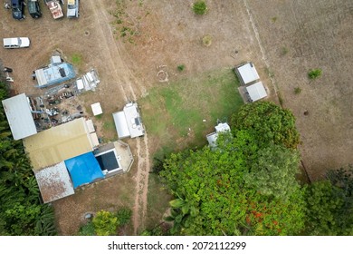 Birds eye view of a shed with junk behind it and a swimming pool in front with vehicles scattered around including cars and caravans, Australian acreage back yard