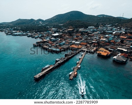 A bird's eye view of a ship navigating fishing boats moored to the docks, with village houses sprawling between the harbor
