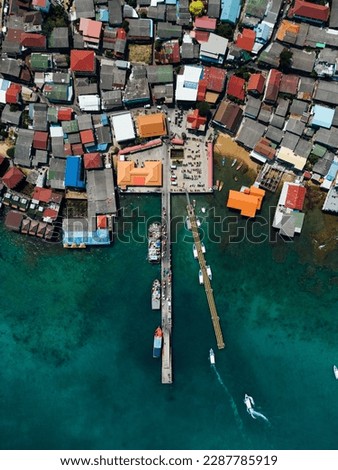 A bird's eye view of a ship navigating fishing boats moored to the docks, with village houses sprawling between the harbor