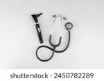 Birds-eye view of essential medical doctor tools, centered and isolated on a white background. Otoscope used for examining inside patients ears and a stethoscope for listening to internal body sounds.