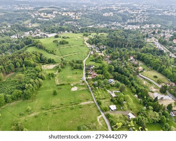 Bird's-eye view of green fields, patchwork farmland, scattered houses along winding roads, and clusters of trees in a peaceful rural landscape. Distant city