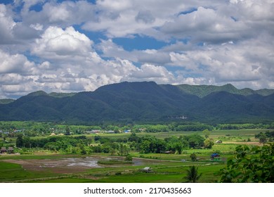 A bird's-eye view of a small village in the countryside Surrounded by mountains and nature in the rainy or farming season of Lampang Province, Thailand.