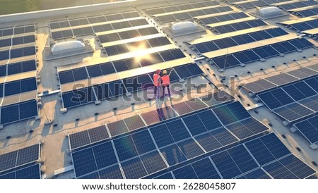 A bird's-eye view of two workers in orange vests on a vast solar panel field, symbolizing eco-friendly energy and green technology.