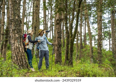Birdwatcher man using binocular searching for birdwatching in green nature forest with hiker woman 