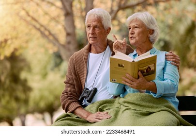 Birdwatching, book and binoculars with a senior couple sitting on a park bench together in nature. Forest, love and retirement with a mature man and woman in a garden to relax with a summer view - Powered by Shutterstock