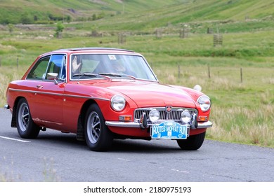 Birkhill, Scotland - JUNE 25, 2022:  Red MG MGB GT Sports Car With Driver And Passenger Waving In A Classic Car Rally En Route Towards The Town Of Moffat, Dumfries And Galloway