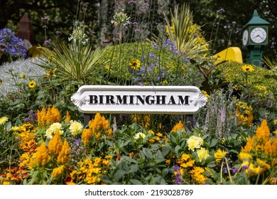 Birmingham city sign surrounded by flowers in garden of city centre park. Old black text on white background metal signage.