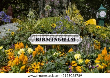 Birmingham city sign surrounded by flowers in garden of city centre park. Old black text on white background metal signage.