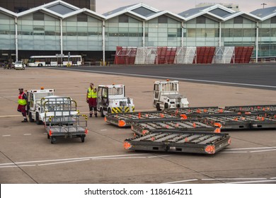 BIRMINGHAM, ENGLAND - SEPTEMBER 2018: Small Tractor Vehicles And Air Freight Pallet Trailers In Front Of The Terminal Building At Birmingham Airport.