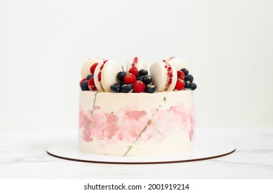 Birthday or anniversary cake with cream cheese frosting decorated with macaroons, blueberries and raspberries. Gold splash on the wedding cake. White background
