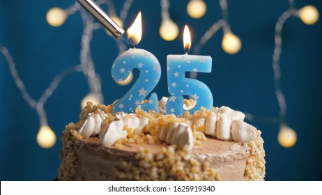 Birthday cake with 25 number candle on blue backgraund set on fire by lighter. Close-up view