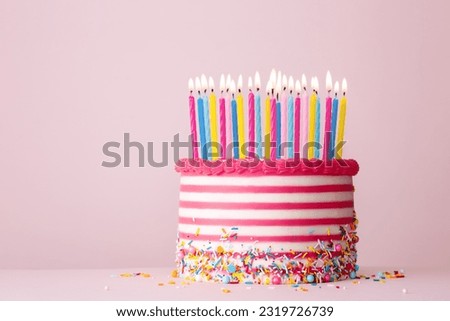 Birthday cake decorated with pink and white striped buttercream and lots of birthday candles against a pink background