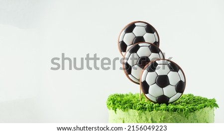 Birthday cake for a football fan with green cream cheese frosting, grass and soccer balls gingerbread cookies on top. White background
