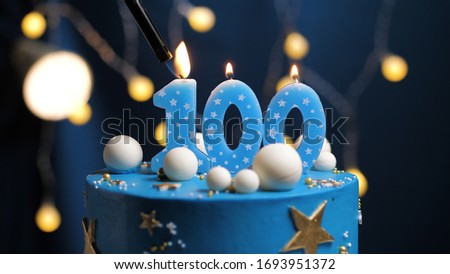 Birthday cake number 100 stars sky and moon concept, blue candle is fire by lighter. Copyspace on right side of screen. Close-up view