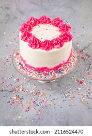 Birthday Cake With Pink And White Buttercream Icing And Colorful Sprinkles Over A Light Grey Background From Overhead.