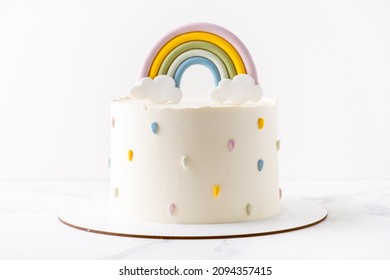 Birthday cake with white cream cheese frosting decorated with colorful mastic rainbow on the white background