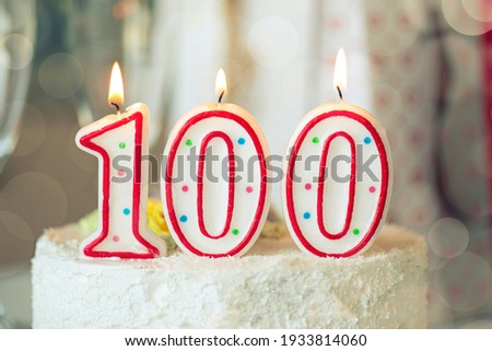 Birthday candle as number one hundred on top of sweet cake on the table, 100th birthday