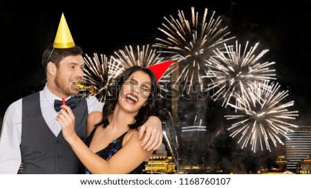birthday, celebration and holidays concept - happy couple with party blowers and caps having fun over firework lights at night city background