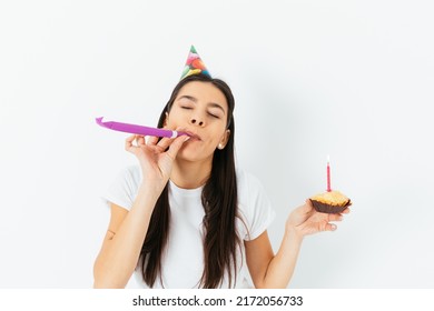 Birthday Celebration, Young Woman In Party Cap Blowing Kazoo Holding Cake With Candle In Her Hand, White Background