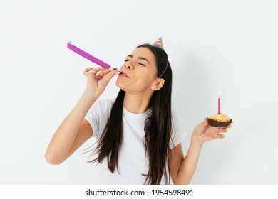 Birthday Celebration, Young Woman Wears Party Hat Blowing In Kazoo Holding Cake With Candle, White Background