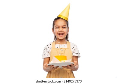 birthday, childhood and people concept - portrait of smiling little girl in dress and party hat with cake over white background