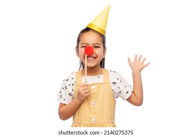 Birthday, Childhood And People Concept - Portrait Of Little Girl In Dress And Party Hat With Red Clown Nose Over White Background