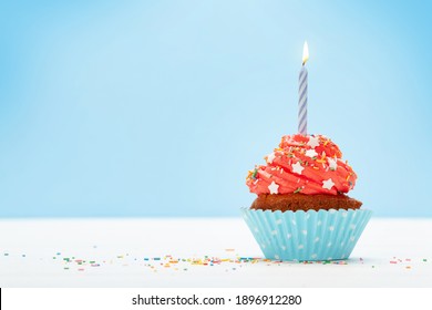 Birthday cupcake with burning candle over blue background with copy space for your greetings