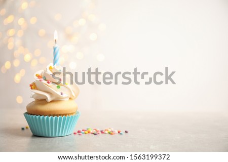 Birthday cupcake with candle on light grey table against blurred lights. Space for text