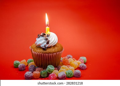 Birthday Cupcake With Candle On Top And Candies With Red Background