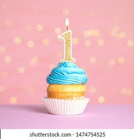 Birthday cupcake with number one candle on table against festive lights