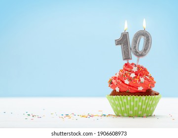 Birthday cupcake with number ten burning candle over blue background with copy space for your greetings