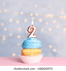 Birthday cupcake with number two candle on table against festive lights