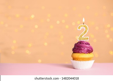 Birthday cupcake with number two candle on table against festive lights, space for text