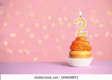 Birthday cupcake with number two candle on table against festive lights, space for text
