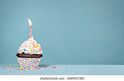 Birthday Cupcake With Sprinkles And A Candle Over A Blue Background.