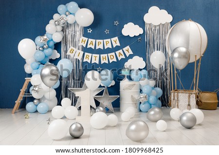 Birthday decorations - gifts, toys, balloons, garland and figure for little baby party on a blue wall background.