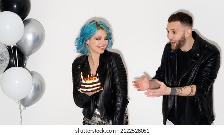 Birthday Fun. Happy Friends. Festive Surprise. Party Celebration. Funny Shocked Man Wishing Holiday Cake With Candle Lights In Hands Of Playful Woman Isolated White Black Silver Balloons Decor.