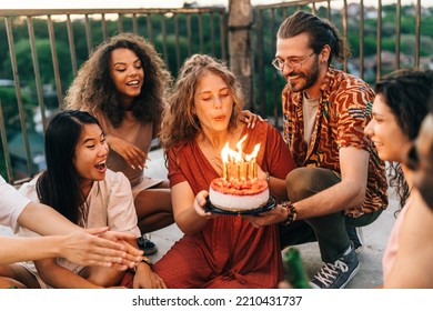 A birthday girl blows candles and wishes a wish while her friends look at her. A man holds a birthday cake while a girl blows the candles. The rest of the crew smiles and looks at her.