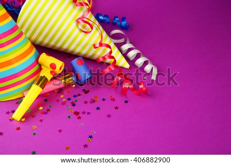 Birthday hats with serpentine streamer and noise makers on purple background
