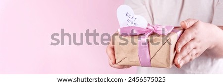 Birthday, Mother's Day international holiday greeting card. Child's hands holding a bouquet with wild flowers daisies and a gift box with a ribbon, on a pink background  copy space