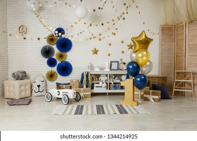 Birthday Navy Blue And Gold Decorations With Gifts, Toys, Garlands And Figure For Little Baby Party On A White Bricks Background.
