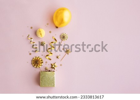 Birthday objects exploding from a gold sparkly gift box, overhead view, against a pink background