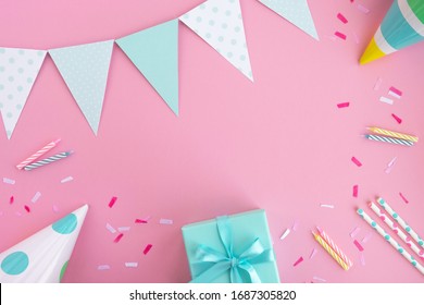 Birthday party background. Composition in pastel pink and mint colors. Birthday caps, gift box, party flags, drinking straws, confetti and candles. Top view, flat lay, copy space