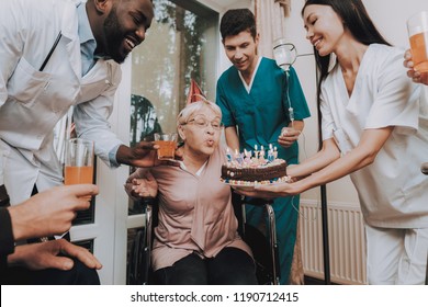 Birthday Party. Celebration. Gifts. Balloons. Guests. Group. Young And Old People. Nursing Home. Congratulate. Elderly Woman. Birthday. Very Surprised. Very Happy. Glasses Of Drinks. Nurse Hold Cake.